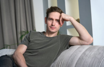 calm relaxed man is sitting on couch at home in living room looking at camera